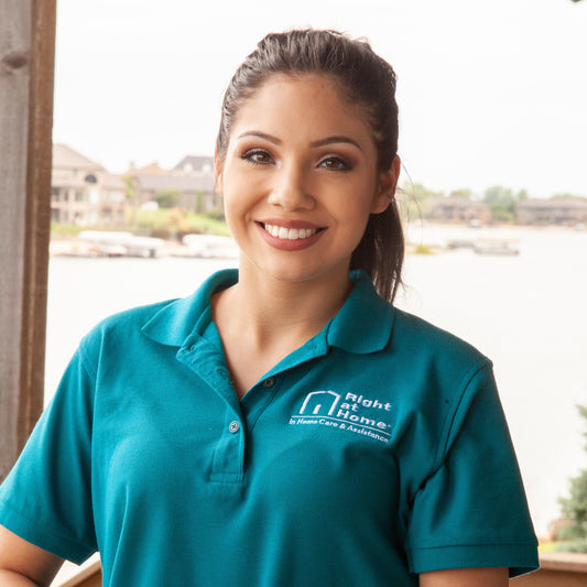 Woman wearing a teal shirt with a logo, standing on a balcony with a scenic background